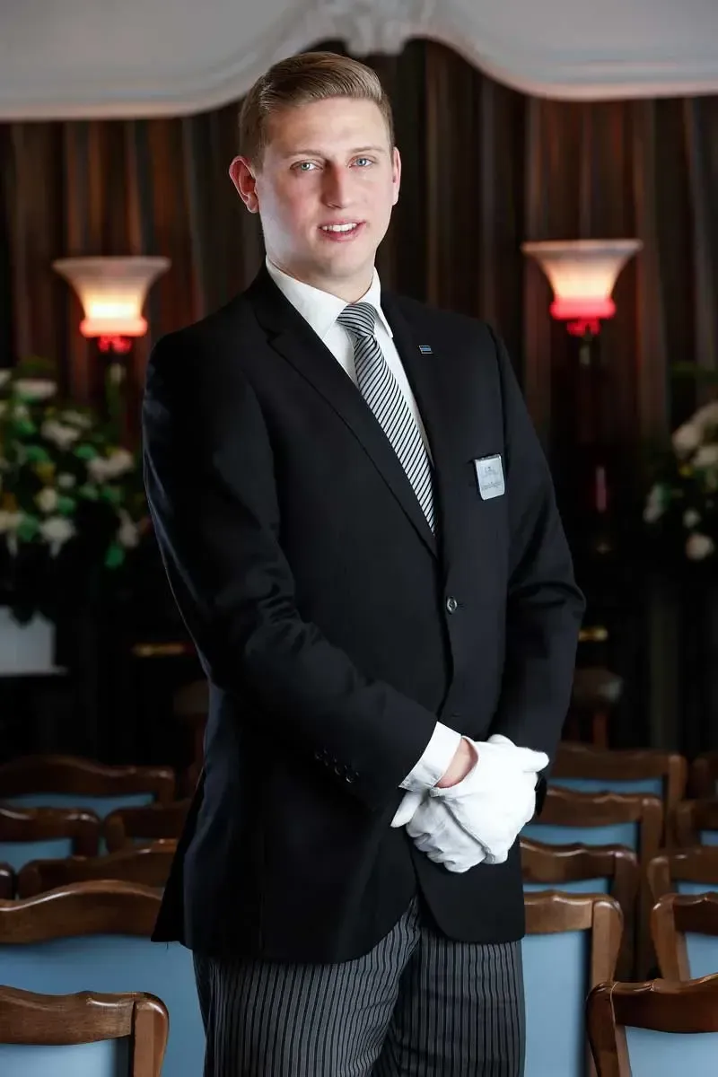 Man in black suit and white gloves standing in a formal dining room