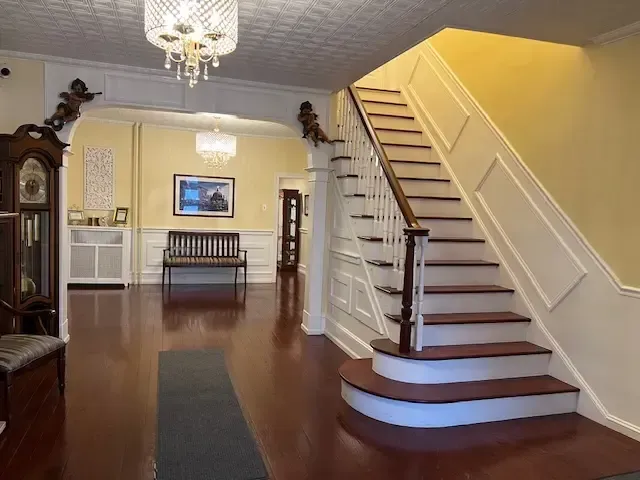 Foyer with polished wood floors, staircase on the right, chandelier, and antique clock on the left.