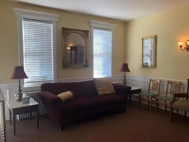 Living room with burgundy sofa, two lamps, wall mirror, and chairs by a window