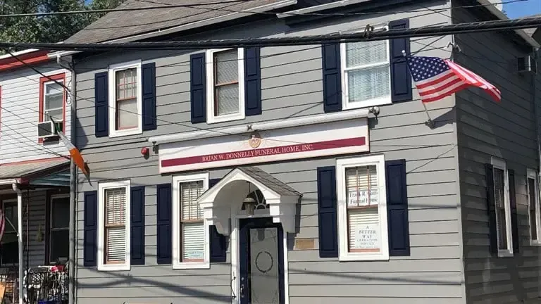 Gray two-story house with black shutters and a front porch, displaying an American flag