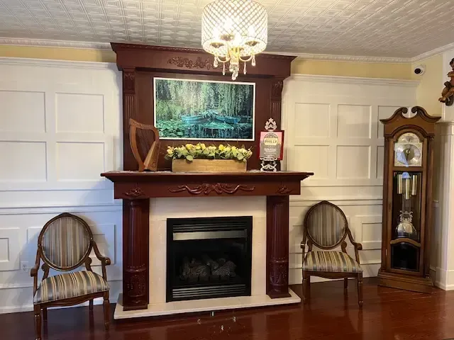Living room with fireplace, chandelier, two wicker chairs, and a grandfather clock
