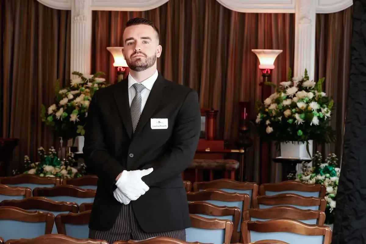 Hotel staff member in a black suit and white gloves standing in an elegant banquet hall