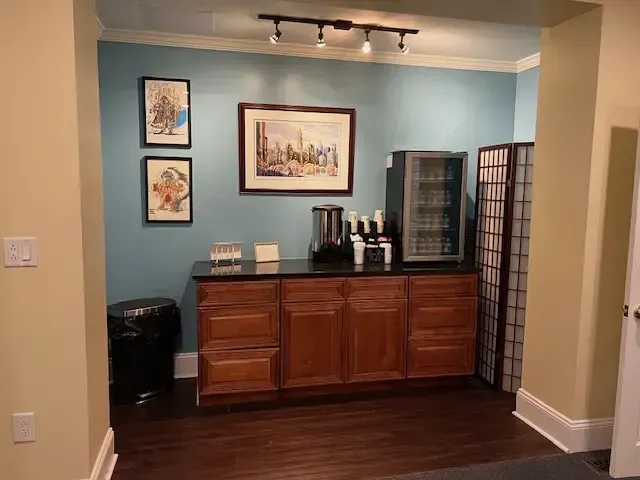 Dining nook with a wooden cabinet, coffee station, blue walls, framed art, and a folding privacy screen.