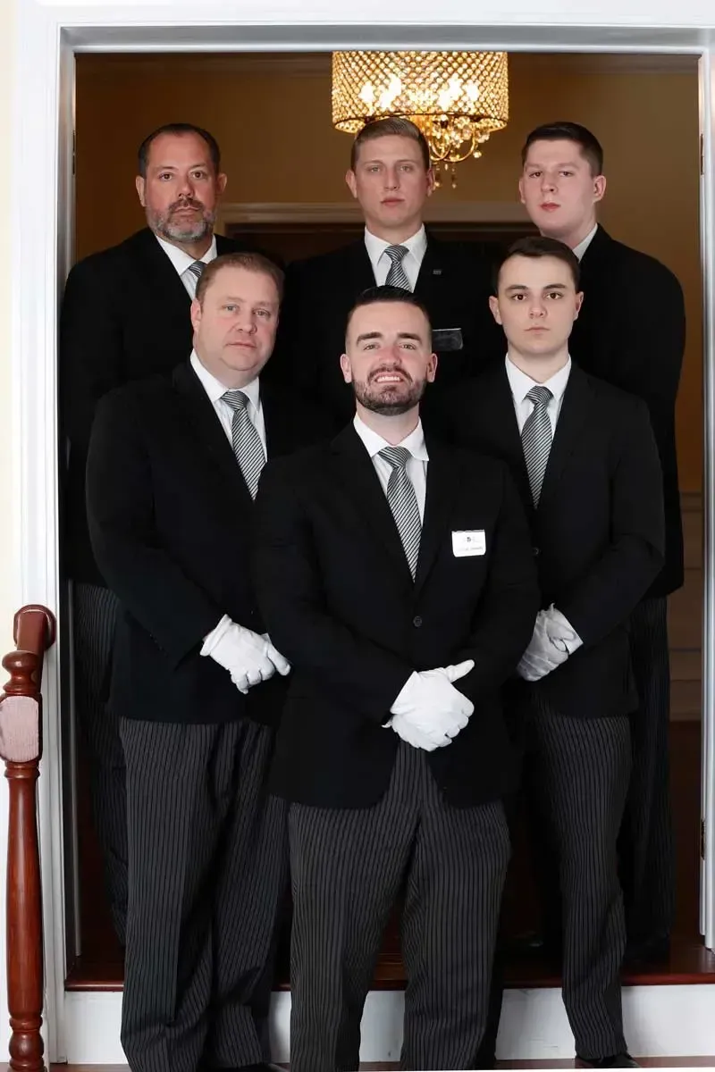 Five formally dressed men pose in a doorway, one seated in front and four standing behind.