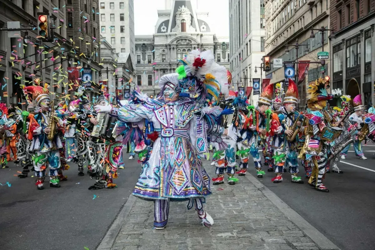 Colorfully costumed dancers parade down a city street during a festive carnival.