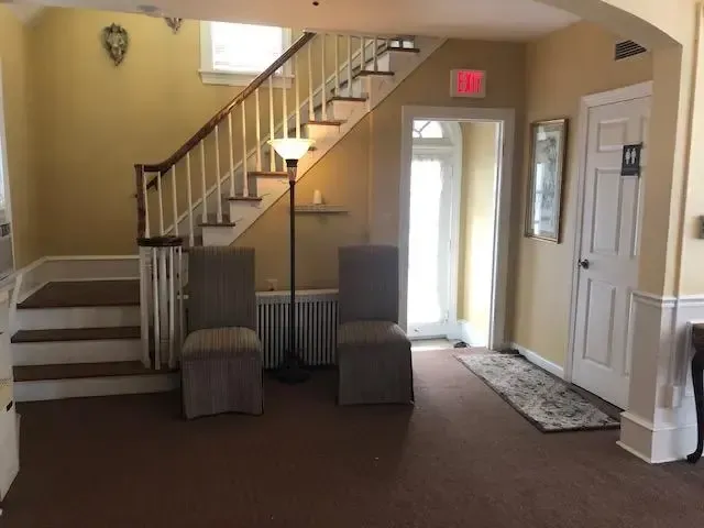 Small lobby with staircase, two chairs, front door, and beige walls.