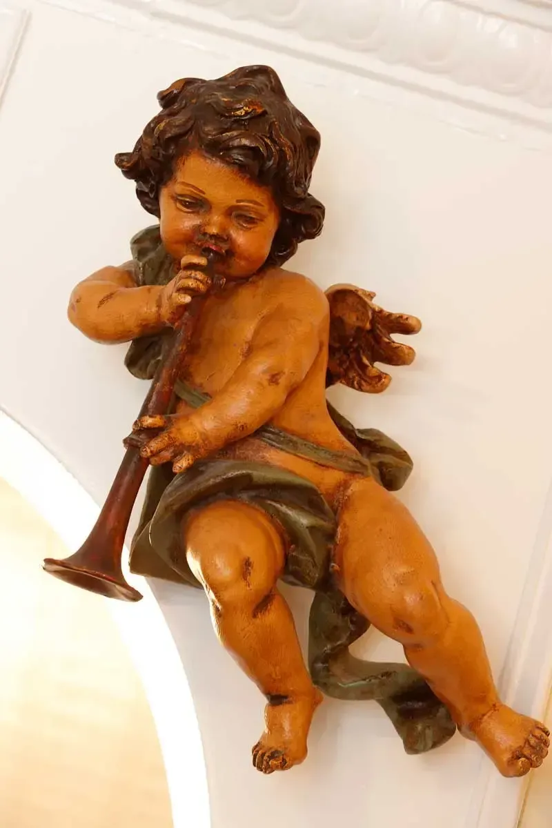 Small cherub figurine playing a trumpet, reclining on a white surface.