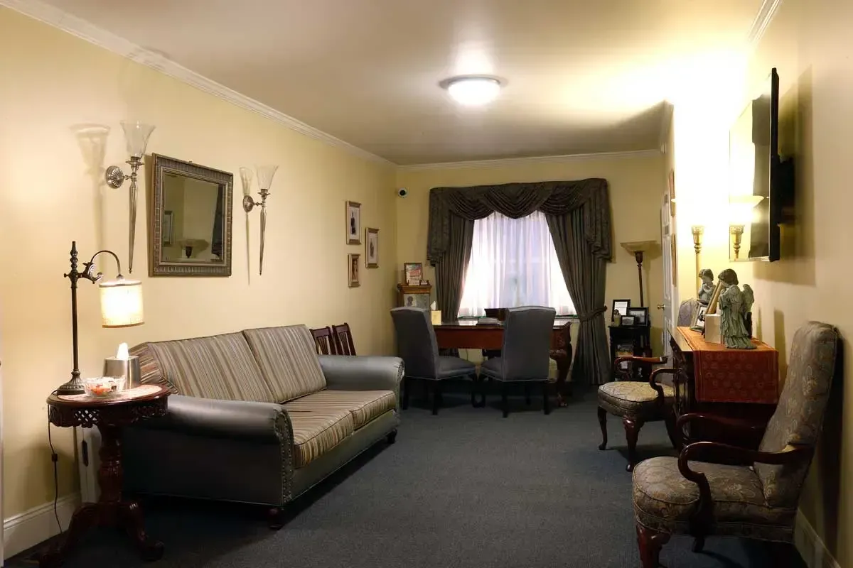 Cozy living room with beige sofa, lamps, framed wall art, and a window with curtains.