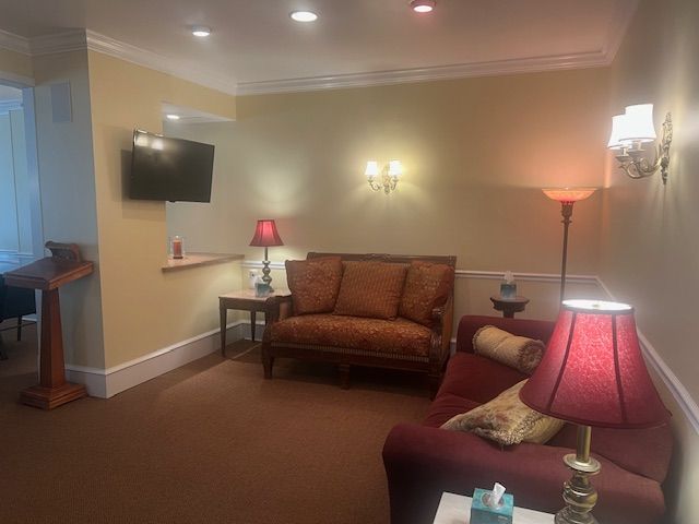 Cozy living room with brown sofa, armchair, wall-mounted TV, and warm lamps on beige walls.