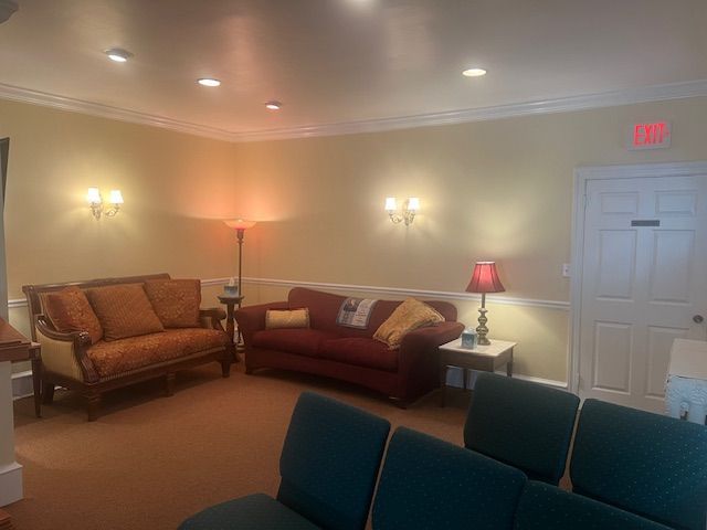 Quiet waiting room with tan walls, brown sofas, teal chairs, lamps, and a white door.