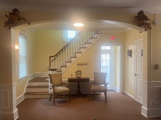 Bright foyer with staircase, round table, chairs, and arched entryway under warm lighting