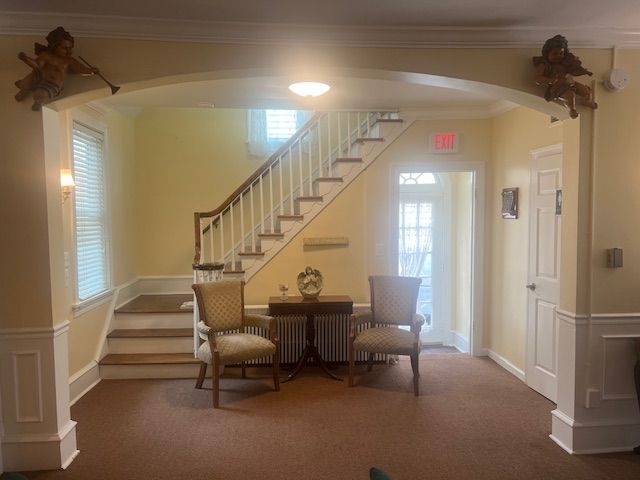 Bright foyer with staircase, small table and chairs, beige walls, and front door with glass panes