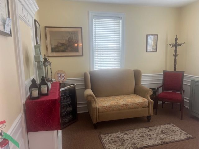 Small beige living room with sofa, red chair, side table, wall art, and window blinds