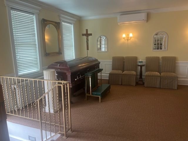 Small chapel room with a casket, cross, chairs, and wall sconces under soft light