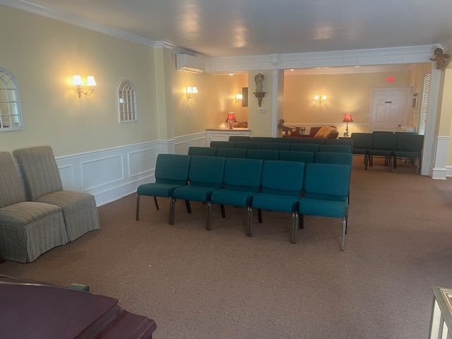 Empty chapel with teal pew chairs, beige walls, wall sconces, and a small altar at the back.