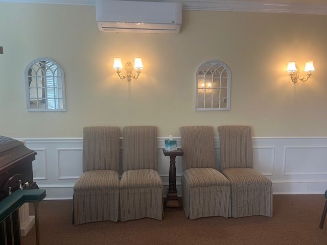 Quiet room with four striped chairs, wall sconces, and arched windows beneath an air conditioner.