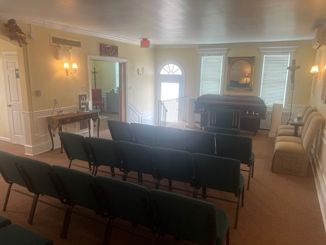 Small chapel seating area with rows of green chairs and a piano at the front.