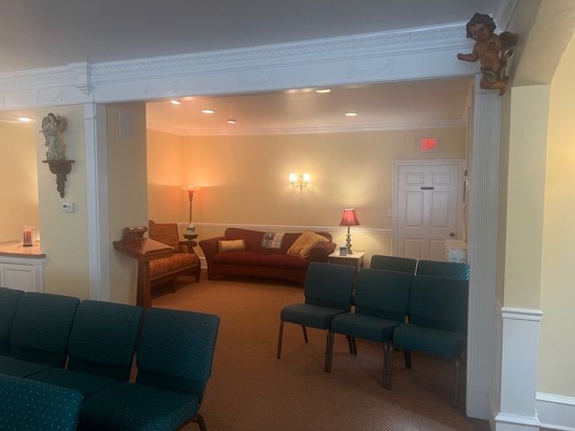 Quiet meeting room with green chairs, a couch, and warm wall lamps under a white archway.