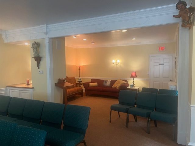 Quiet lounge with green chairs, sofa, lamps, and a white doorway under warm lighting.
