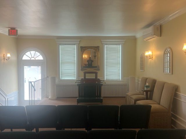 Quiet meeting room with rows of chairs, a podium, and wall sconces beside a front door and windows.