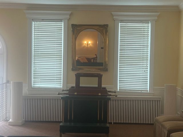 Elegant living room wall with centered mirror, twin windows, radiator cover, and beige sofa edge