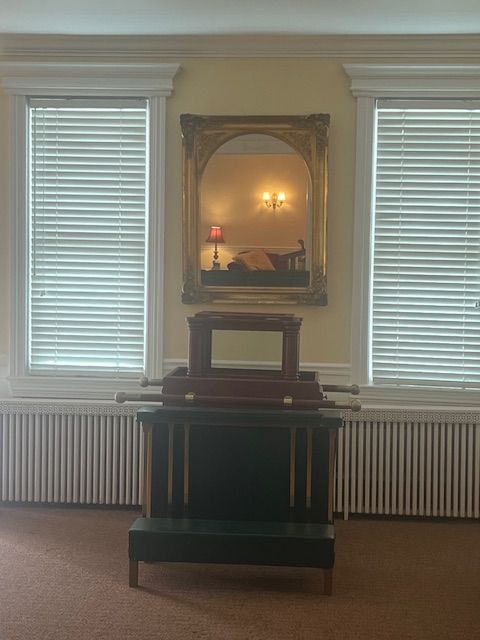 Dim room with two windows, a radiator, a framed mirror, and a dark cabinet centered below it.
