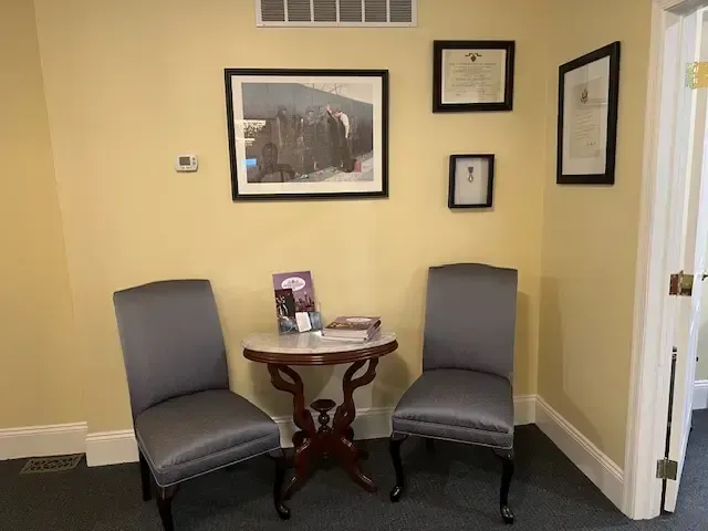 Two gray chairs beside a small round table in a beige waiting area with wall art and framed certificates