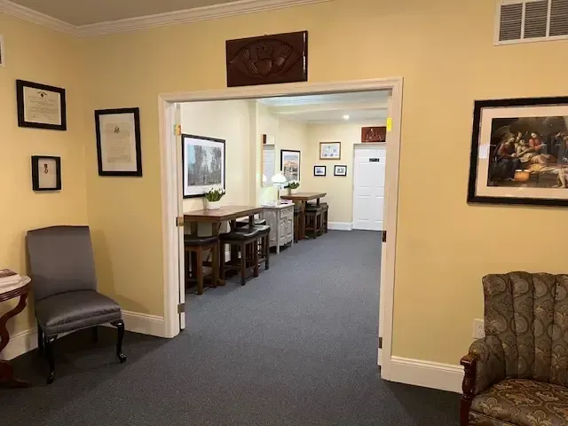 Waiting room hallway with beige walls, chairs, framed art, and tables leading to a back office.