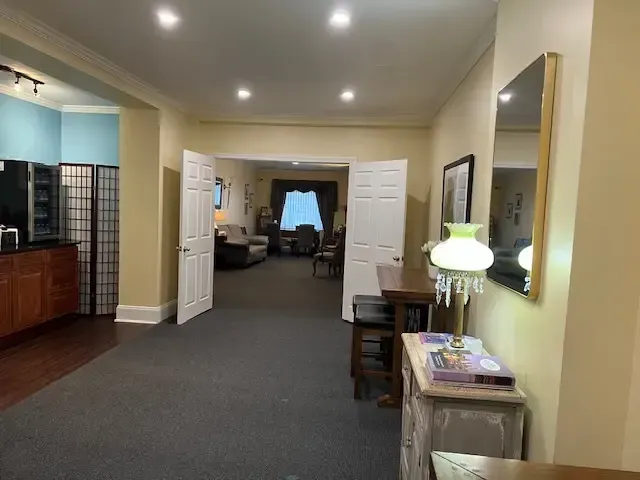 Spacious hallway with dark carpet, open double doors, and a small table with lamp and books on the right