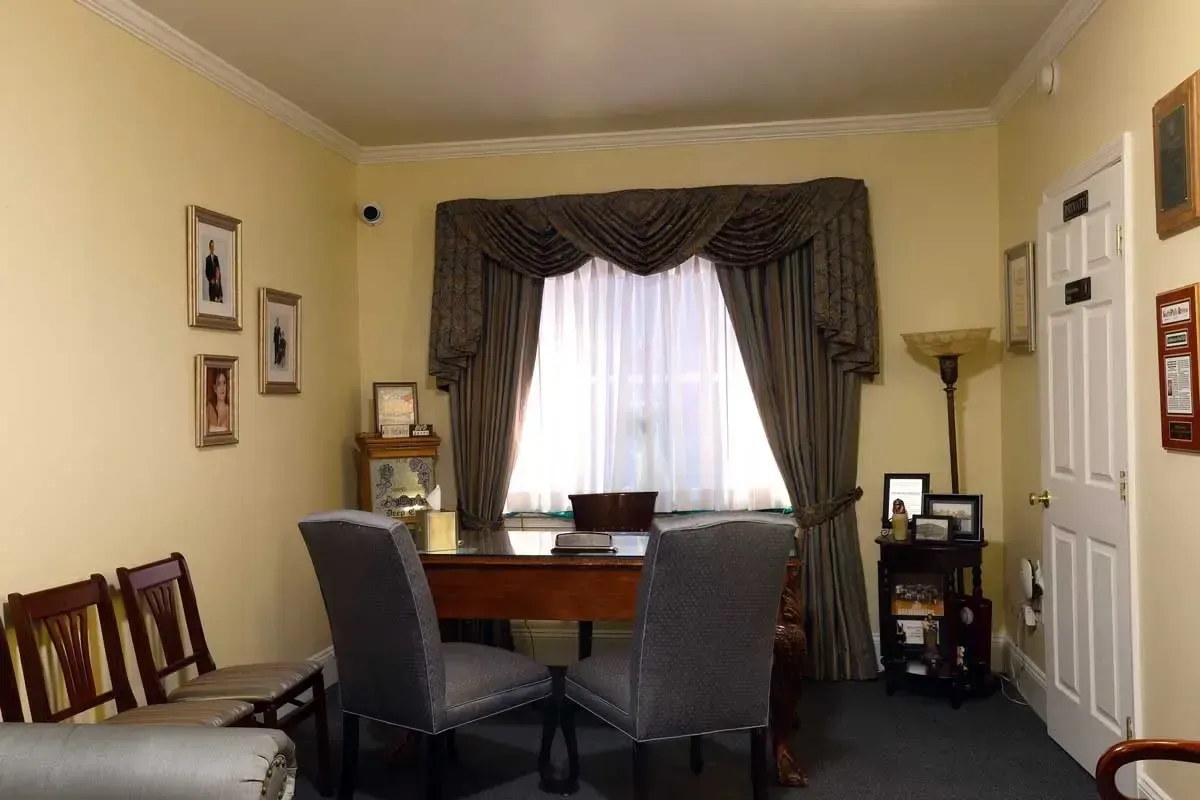 Home office with desk, two chairs, window curtains, framed photos, and closet doors.