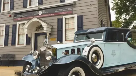 Vintage blue classic car parked in front of a historic building with a sign above the entrance