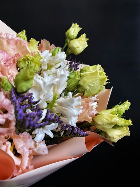 Bouquet of pink, white, and purple flowers wrapped in peach paper against a black background