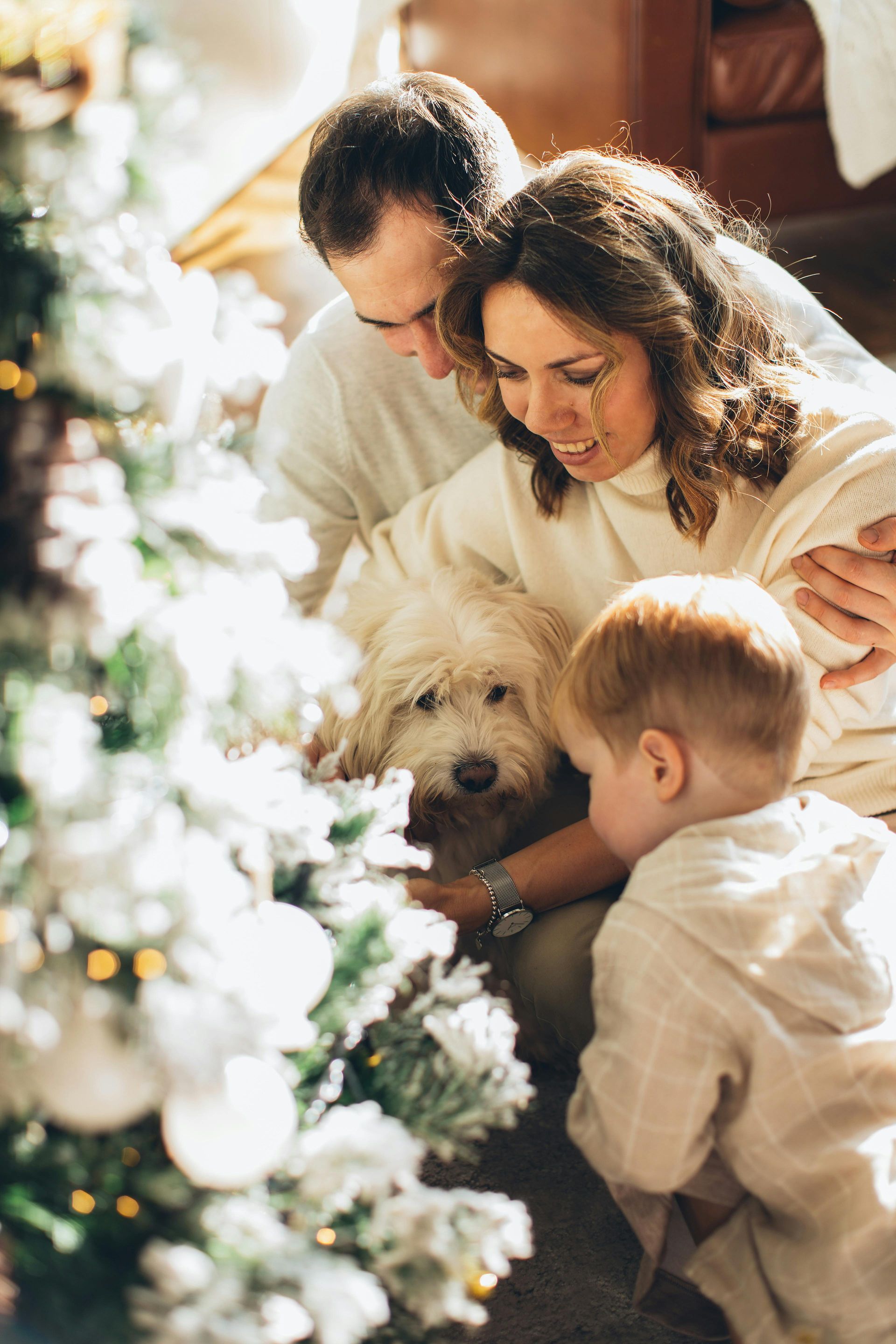 Family gathered around a decorated Christmas tree with a small dog in a cozy, warm-lit room