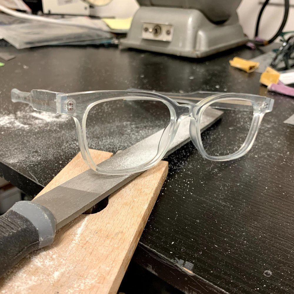 Clear eyeglasses resting on a workbench beside a file and dust-covered surface.