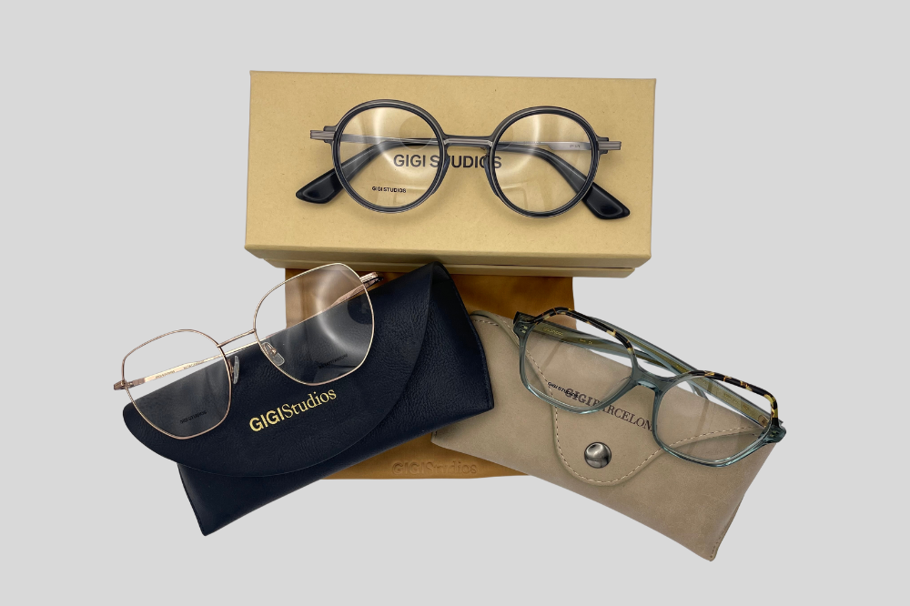 Two pairs of eyeglasses, one blue and one gold, in front of a Gigistudios box