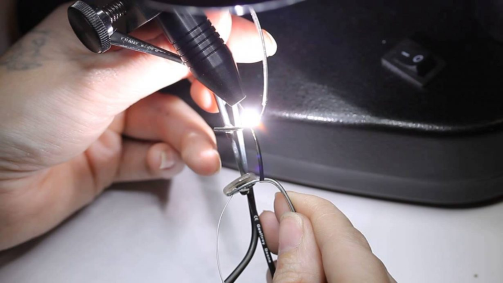 Hands soldering a small wire under a bright task light on a workbench