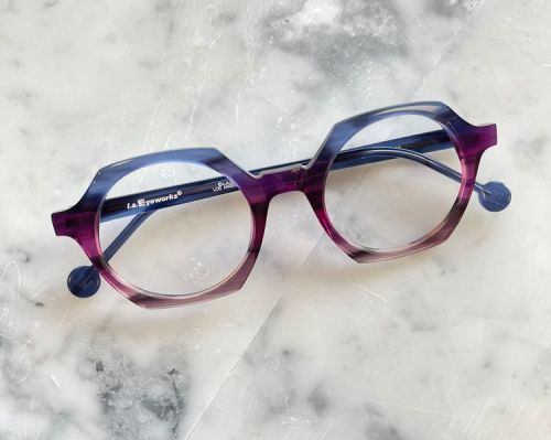 Purple and blue eyeglasses with round lenses on a light marble surface