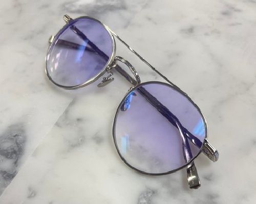 Silver round eyeglasses with blue-tinted lenses on a white marble surface