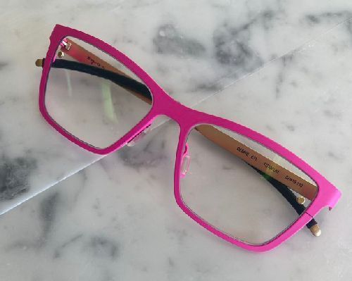 Bright pink eyeglasses with clear lenses on a white marble surface