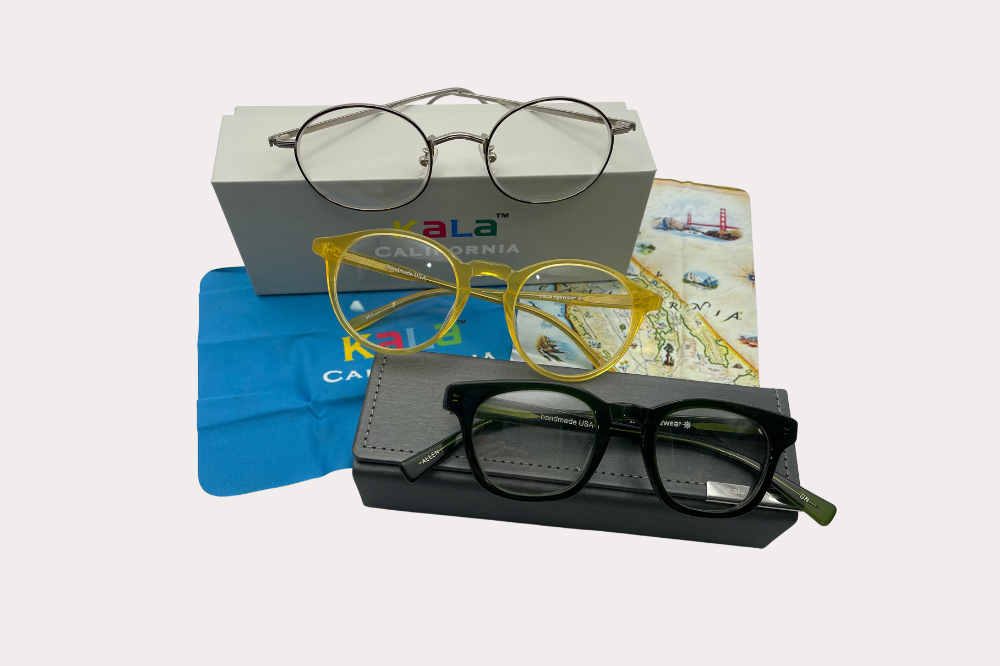 Three pairs of eyeglasses on a white surface, with black, purple, and patterned frames beside a colorful card.