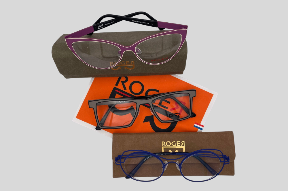 Assorted eyeglasses arranged around an orange card with the word “ROGER.”