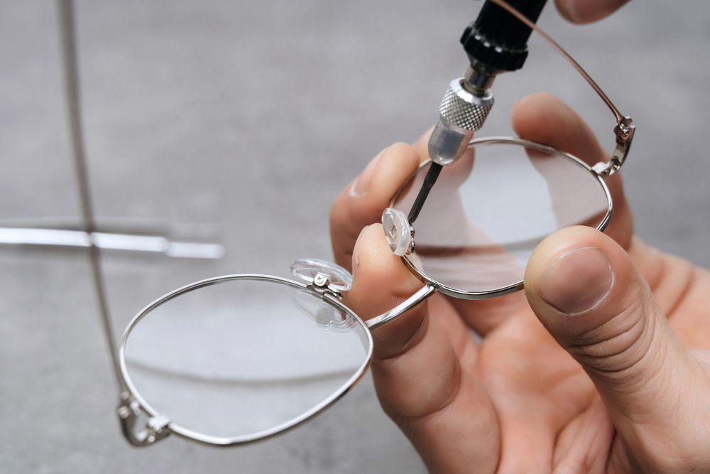 Hands using a tool to adjust metal eyeglass frames on a workbench