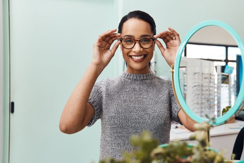 Smiling person adjusting glasses in front of a round mirror in a bright room