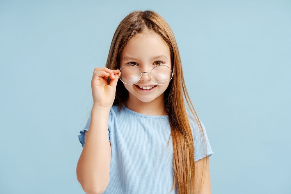 Smiling child in a light blue shirt holding glasses against a blue background