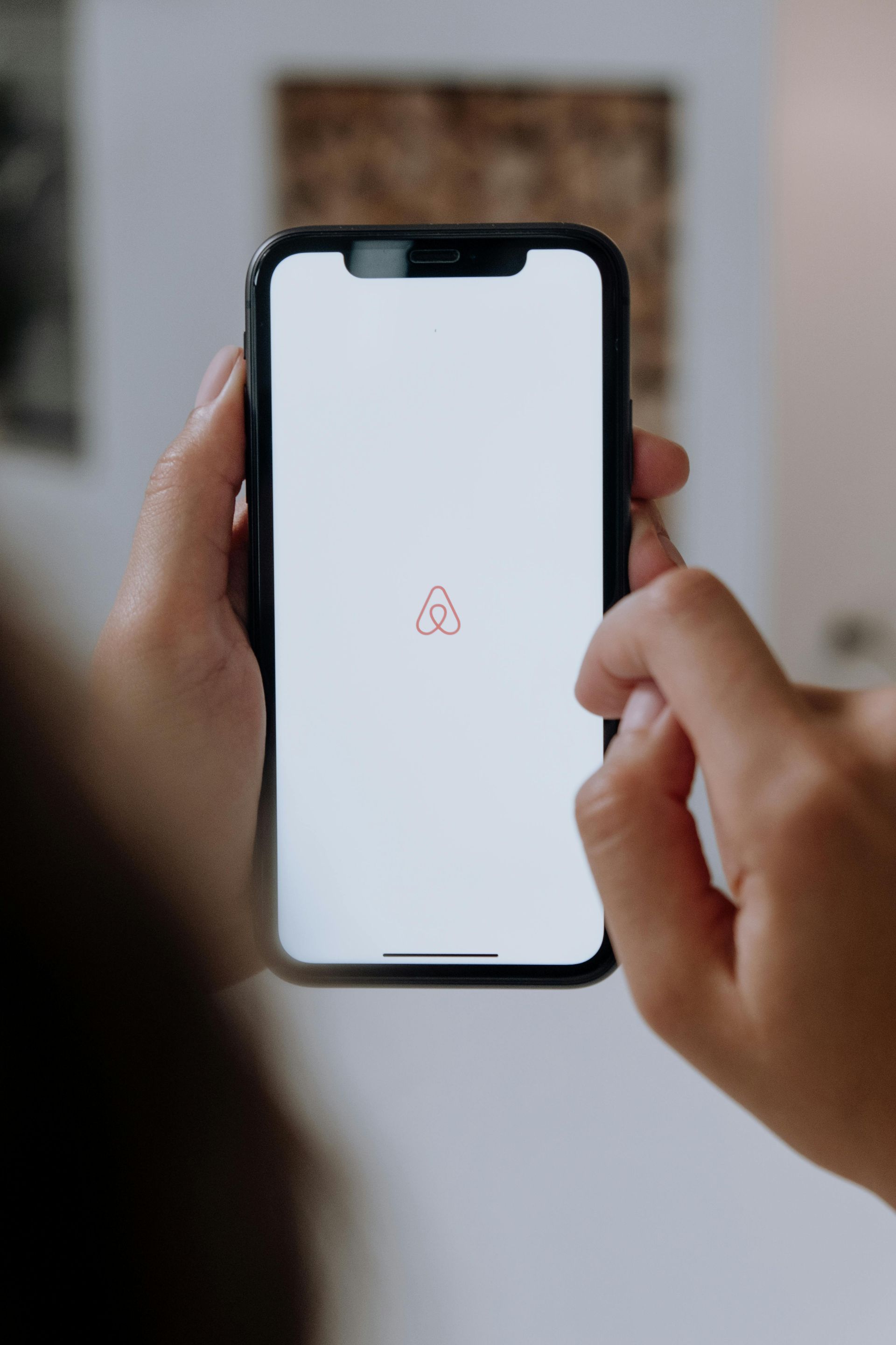 Hands hold a smartphone displaying an Airbnb logo on a loading screen.