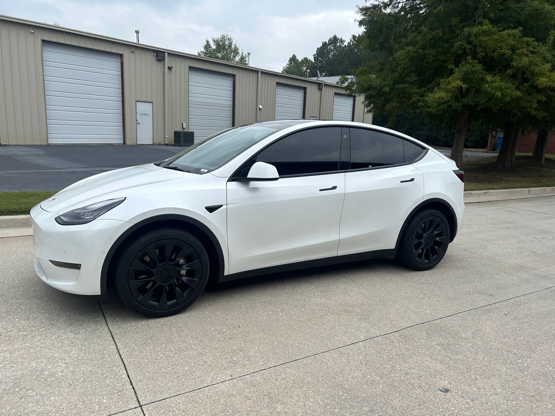 A white tesla model y is parked on the side of the road in front of a building.