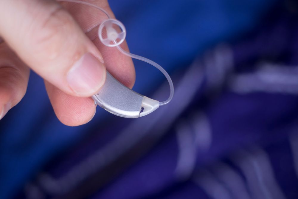 Hand Holding a Clear Hearing Aid With a Thin Wire — Local Hearing Aid Specialists in Wallsend, NSW
