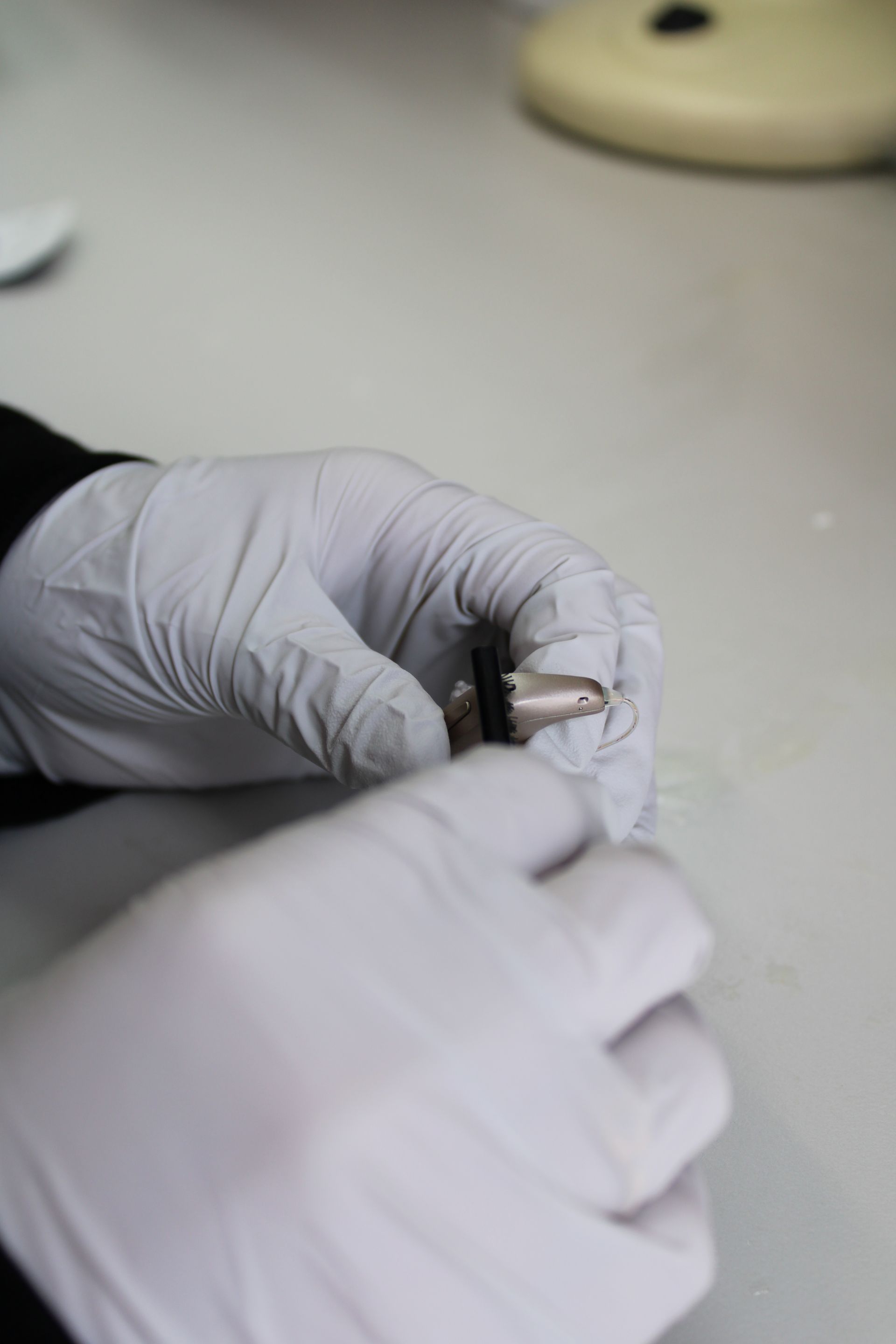 Gloved hands handling a small metal tool on a lab bench — Local Hearing Aid Specialists in Wallsend, NSW