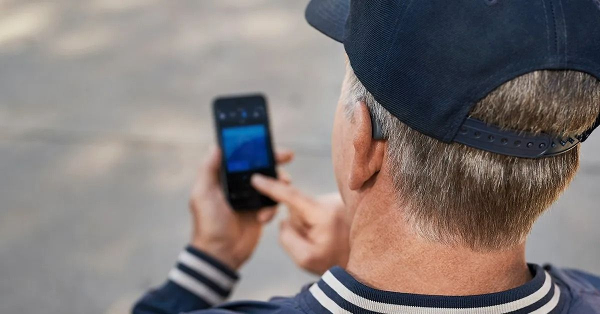 Person in a Navy Cap Holding a Smartphone — Local Hearing Aid Specialists in Wallsend, NSW