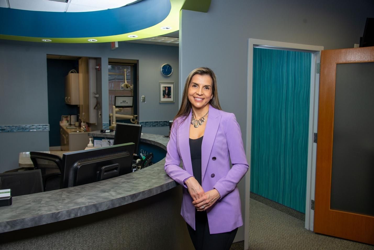 A woman in a purple jacket is standing in front of a counter in a dental office.